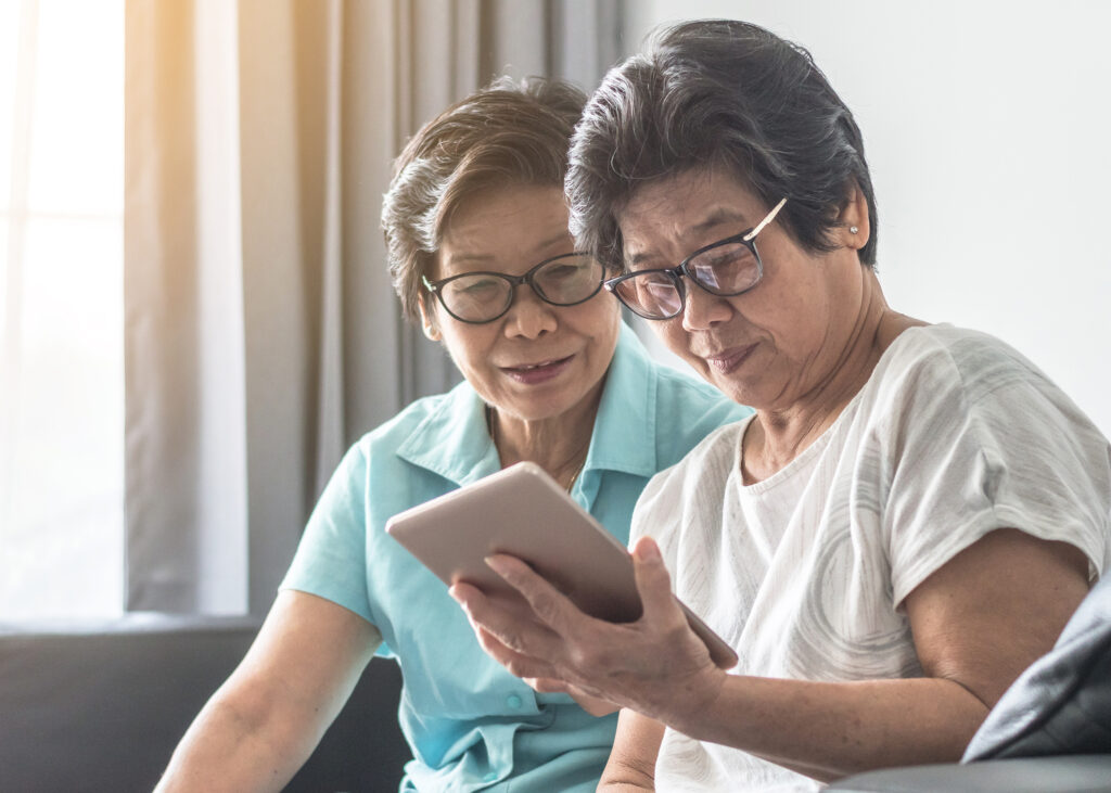 Aging society concept with Asian elderly senior adult women twin sisters using mobile digital tablet application technology for social media network among friends community via internet communication