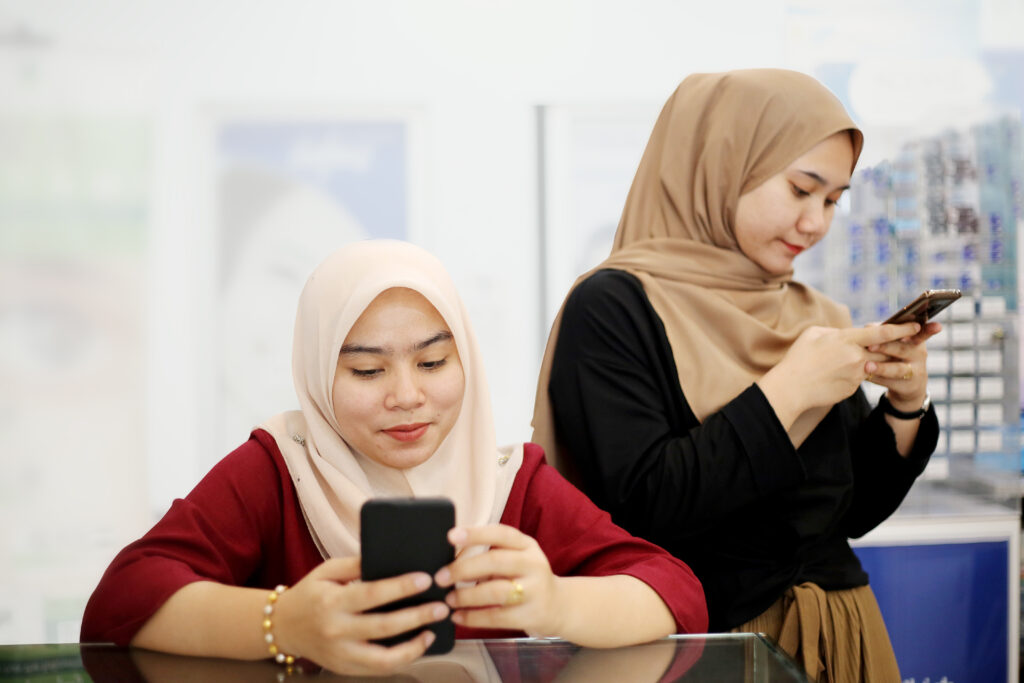 Two Muslim female adults are enjoying using smartphone for online messaging in optometry.